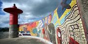 Photo of the light beacon that sits at the end of the Eisenhower Pier alongside a mosaic mural depicting the boroughs role in WWII