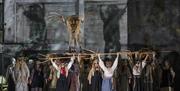 The NI Opera Chorus dressed as peasants and wearing rustic masks, holding pitchforks raised in the air, on stage in the Grand Opera House for Eugene O