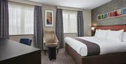 Photo of an executive room in Holiday Inn Belfast City Centre. There is a king size bed on the left side with a frame over the headboard. There is a c