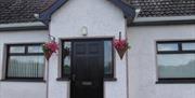 Image of the front of a white bungalow with flower baskets hanging on either side of the door