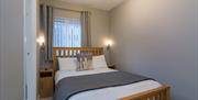 A photo of a small bedroom with a double bed, bedside cabinets and a window.