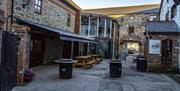 Image is of courtyard area with barrels for tables and a couple of picnic tables.