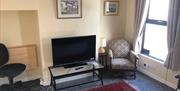 Carpeted living room with a chair, TV and a desk area.
