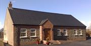 Image shows front of detached cottage which has 6 windows and front door with a few low steps