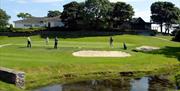 Image is of golf course with golfers playing and lake in the foreground