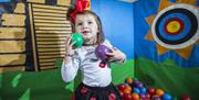 Image is of a young girl playing with coloured balls in a pen