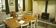 A dining room with stone tiles, a woodburning fireplace, and a table and chairs.