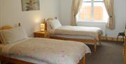 image shows twin bedroom with side table, lamp and window