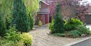 A pebble path leading to a front entrance on a private road decorated with trees and bushes.