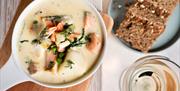 A bowl of seafood chowder, with two slices of wheaten bread and a glass of wine next to it.