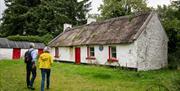 A mature couple walking towards an Irish thatched white cottage with red door.