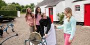 Girls pictured with a woman in period dress outside an old thatched cottage with a red door