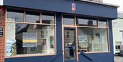 Exterior of the Gallery in Whitehead, painted blue with large windows and art displayed in them