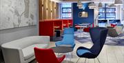 Photo of the lobby in Holiday Inn Express Belfast City. Blue and red chairs, coffee table and grey sofa in the foreground, with map of Belfast on the