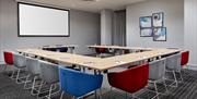 Photo of a meeting room in Holiday Inn Express Belfast City. The room is in U-shape style with stylish red, blue and grey seats. Tables are set with c
