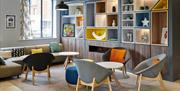 Photo of the lobby in Holiday Inn Belfast City Centre. Corner sofa with chairs and coffee tables. One wall has a large unit with built-in fireplace an