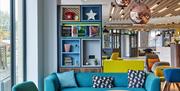 Photo of the lobby in Holiday Inn Belfast City Centre. Blue sofa with coffee tables in the foreground. Wall element with colourful niches with decorat
