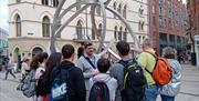 A tour group listening to a guide at a sculpture in Belfast city centre.