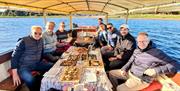 a group onboard ariver boat with various trays of food sat on the table infront of them