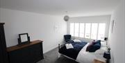 Double bedroom with a chair, wardrobe/drawers, and panel windows covering the wall.