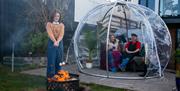 Mother and Daughter being hosted by goldsmith in Igloo.  Daughter roasting marsh mallows over fire pit with mother and goldsmith looking on, enjoying