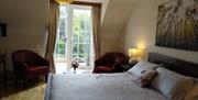 The photo shows a king size bed made up in silver bedlinen and a decorative cushion. On either side of the bed is a dark wood bedside table with a cre