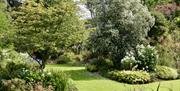 A mowed grass path through a garden with flowers and trees.