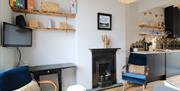 Open plan lounge through to dining kitchen. Pale gray wall, black cast iron fireplace,blue velvet armchairs & grey sofa. Navy kitchen, open shelving a