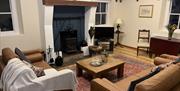 The photo is of the living room of Dunnaglea Cottage. Within the photo are two sofas, a coffee table, a TV, a log burner fire, and a dining table.