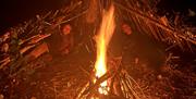 Two women laying under stick huts around a camp fire.