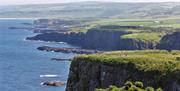 A group of walkers travelling along the rugged coastline cliffs  with the sea below
