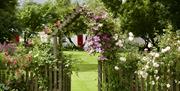 A wooden garden gateway with flowers growing all over.