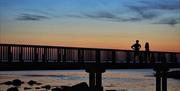 Couple standing on wooden pier looking at the sunset  at Ballycastle Beach.