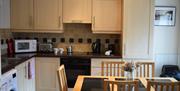 Kitchen with light wood coloured wall and under workbench units. Table and chairs in centre of kitchen