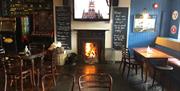 Image is of the lounge area of the bar with open fire blazing and table and chairs