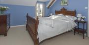 Image shows double bedroom with chest of drawers, beside table with lamp and carpeted floor