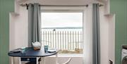 A small dining area with a table set with plates, mugs and a teapot and a large window with a lough view.