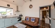 Kitchen lounge area with a brown sofa, coffee table, fridge, hob/oven, sink and a window.