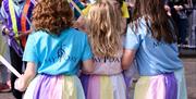 A photo of a trio of little girls taking part in the annual maypole dancing dressed in pastel skirts to match the ribbons of the Maypole