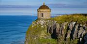 View of Mussenden Temple perched on a dramatic cliff edge above the Atlantic Ocean, seen along the coastal walking trail from Castlerock.