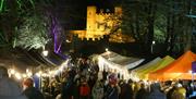 Stalls lined up along the treelined, festively lit, The Dark Walk at Royal Hillsborough Christmas Market with Hillsborough Fort in the background.