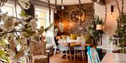 Restaurant with tables and chairs decorated with faux plants and lamps.
