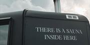 Side of matte black sauna with writing reading "there is a sauna inside here"