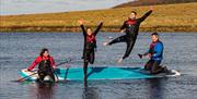 Four people jumping off a paddleboard into water