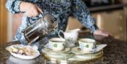 Image with owner pouring tea into cups with buns on a plate