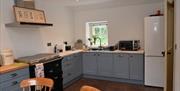 A kitchen with an antique style cooker, sink, microwave and fridge with a window.