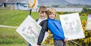 Two children holding poster boards of illustrations by Quentin Blake, in the grounds of WWT Castle Espie