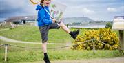 A child jumping up into the air whilst holding a poster board of an illustration by Quentin Blake, in the grounds of WWT Castle Espie
