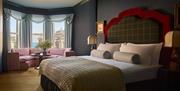 interior of double bedroom at Adelphi Hotel - features a tartan headboard and knitted throw on the bed, as well as a low pink sofa by the window overl