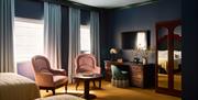 interior of twin bedroom at Portrush Adelphi. Visible is two pink arm chairs and wooden table, a mahogany mirrored wardrobe and a desk with a green va